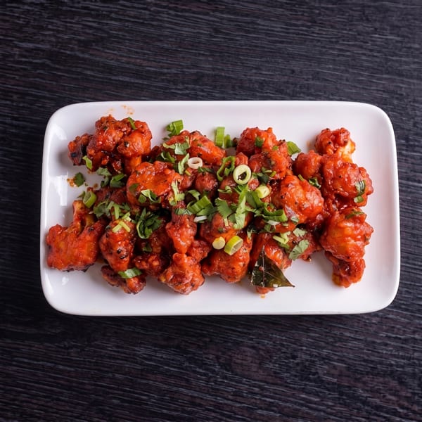 Spicy red cauliflower florets, garnished with fresh green herbs, on a white rectangular plate.