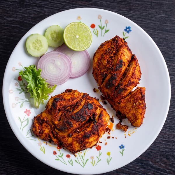 Two pieces of grilled chicken with cucumber, red onion, lettuce, and lime on a white plate.
