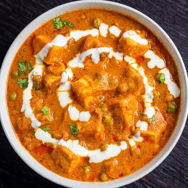 A white bowl filled with vibrant orange paneer butter masala, garnished with cream swirls and cilantro.