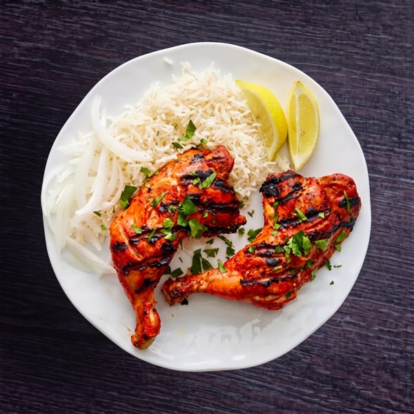 Grilled chicken drumsticks with rice, sliced onions, and lemon wedges on a white plate.