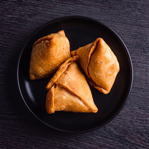 Three golden-brown samosas arranged on a black plate, against a dark wooden background.