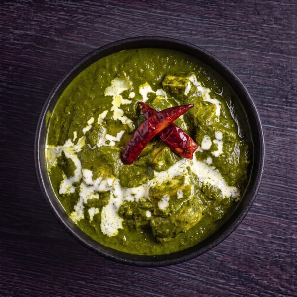 Palak Paneer, a vibrant green spinach and cheese curry, garnished with cream and red chilies.