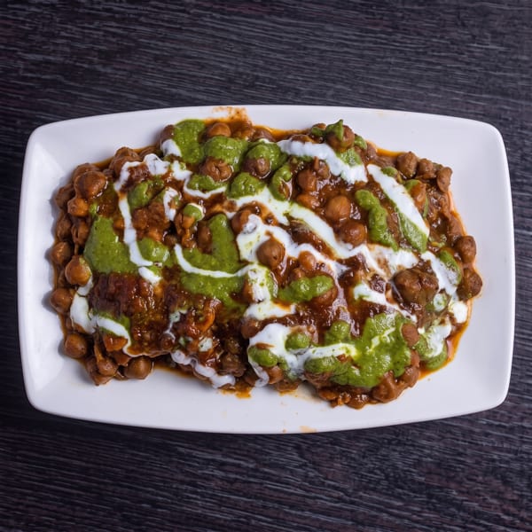 Chana chaat, a chickpea dish, topped with green chutney and white yogurt sauce on a white plate.