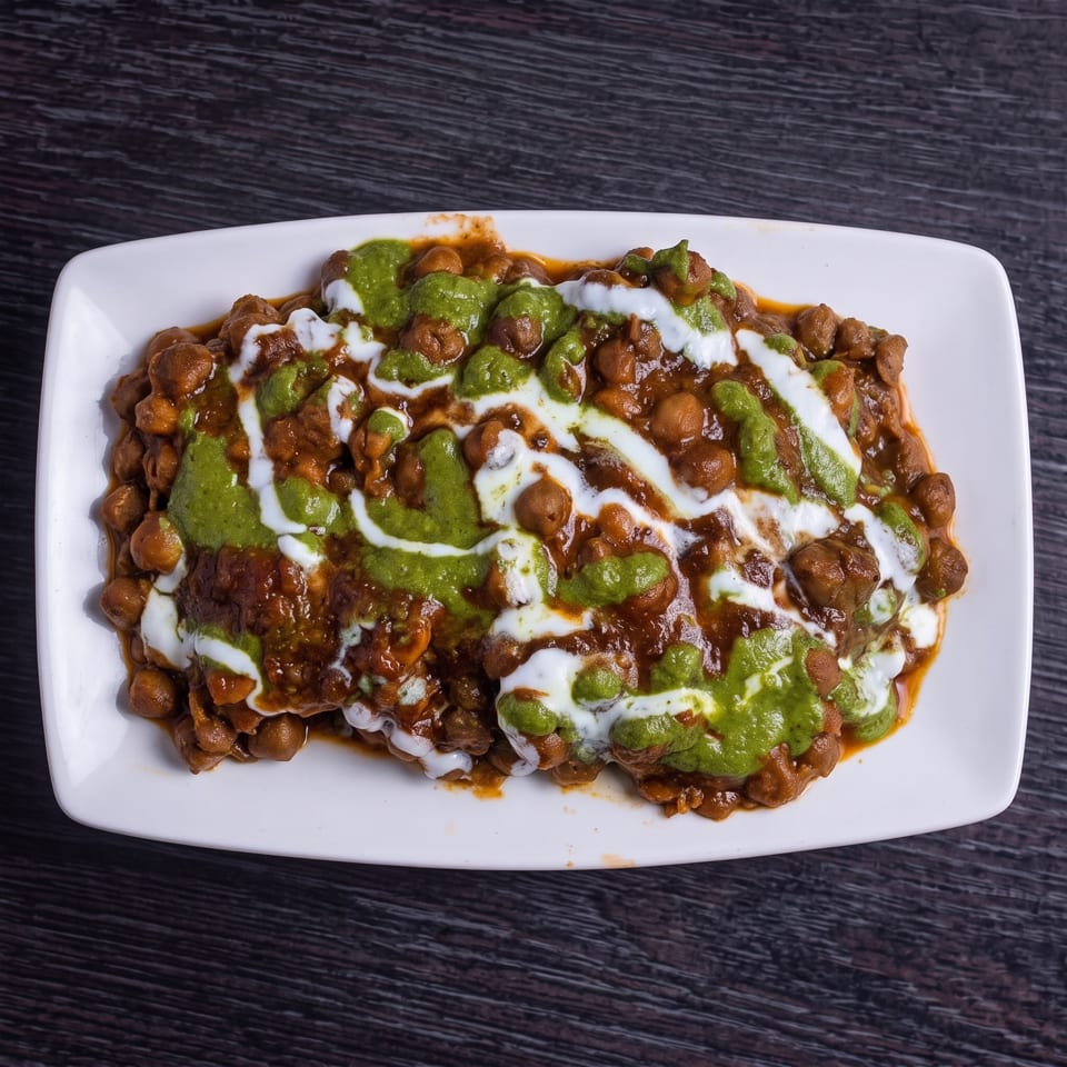 Chana chaat, a chickpea dish, topped with green chutney and white yogurt sauce on a white plate.